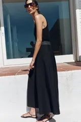 Sandalia plana de color negro con textura efecto piel de serpiente. Presenta una tira central con un aplique metálico dorado curvo y cierre de pulsera con hebilla ajustable en el tobillo.