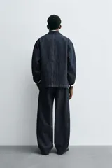 Pantalón de corte barrel fit confeccionado en denim de algodón rígido color azul oscuro. Presenta cintura con pliegues frontales, bolsillos laterales y bolsillos traseros de vivo. Cierre frontal con cremallera y gancho metálico oculto.
