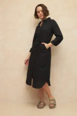 Vestido largo tipo camisero negro, confeccionado en lino, con botones a tono, bolsillos laterales y cinto del mismo material.