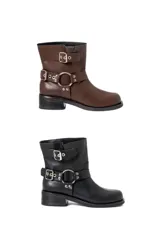 Botas de caña baja de cuero sintético, disponibles en color marrón y negro. Ambas tienen detalles de correas con hebillas y argollas metálicas plateadas alrededor del tobillo y en la parte superior de la caña.