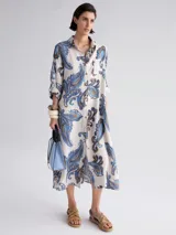 Vestido camisero largo con estampado paisley en tonos celeste, azul y marrón. Tiene cuello camisero, mangas largas con puños abotonados, cierre frontal con botones y un bolsillo en el pecho.