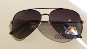 Lentes de sol estilo aviador con montura metálica negra y lentes polarizadas grises.