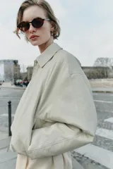 Chaqueta estilo bomber de cuero sintético en color beige, con cuello solapa, cierre frontal con cremallera, mangas largas y bajo elástico fruncido.