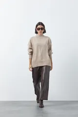 Polera de tejido de punto color gris, con cuello alto, mangas largas abullonadas con puños elásticos y costura central vertical en el frente. Presenta una abertura sutil en la espalda.