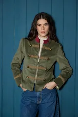 Blazer corto de estilo militar confeccionado en terciopelo verde oliva. Presenta cuello mao en contraste color bordó, cierre frontal con cremallera y botones metálicos decorativos. Incluye detalles de galones bordados en el frente y en los puños.