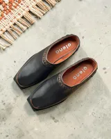 Zueco de cuero color negro con punta cuadrada y detalle de tachas metálicas alrededor de la abertura. Cuenta con plantilla de cuero en color suela y marca grabada.