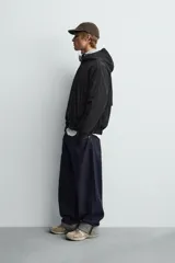 Cazadora relaxed fit color negro, confeccionada en tejido técnico ligero que repele el agua. Cuenta con cuello subido, capucha ajustable, manga larga y cierre frontal con cremallera. El interior está forrado con tejido de estructura abierta y tiene bolsillos frontales ocultos en la costura. Los acabados son elásticos.