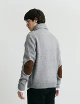 Cardigan de punto color marrón con cuello esmoquin, cierre frontal con botones y presilla superior. Presenta mangas largas con coderas en contraste y bolsillos frontales de ribete.