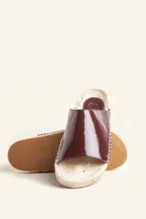Sandalias tipo alpargata con capellada de cuero charol color bordó y planta tejida en fibra natural de yute. Presentan costuras a mano en color blanco y suela de goma.