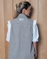 Chaleco de gabardina color tostado, con cuello camisero, cierre frontal con botones metálicos y dos bolsillos frontales con solapa.