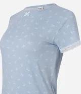 Blusa de pijama de mujer color celeste, confeccionada en tejido peach touch de poliéster con elastano, con estampado de moños sutiles. Presenta cuello redondo, mangas cortas con detalles de encaje blanco y un pequeño moño decorativo en el escote.