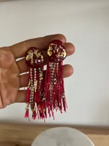 Caravanas artesanales con base superior de resina en color marrón con detalles de lámina dorada y cristales incrustados. Presentan flecos largos de hilo marrón combinados con tiras de strass brillante.