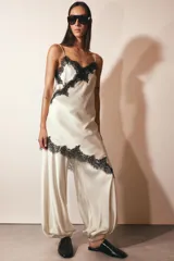 Vestido corto satinado negro con breteles finos, escote en V y bajo asimétrico con abertura. Detalle de encaje en escote y ruedo.