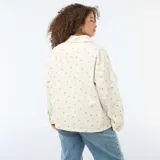 Sobrecamisa de twill color blanco con estampado floreado sutil, corte holgado, cuello camisero, cierre frontal con botones metálicos y dos bolsillos de parche delanteros.