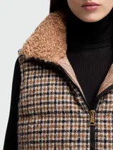 Chaleco acolchado de lana con diseño a cuadros en tonos marrón, beige y negro. Presenta cuello alto, cierre frontal con cremallera y el parche del logo de Moncler en el pecho.