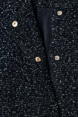 Blazer de cuello redondo y manga larga, confeccionado en tejido de tweed con textura. Presenta un diseño entallado con cinturón forrado a tono con hebilla metálica y cierre frontal mediante botones a presión ocultos.