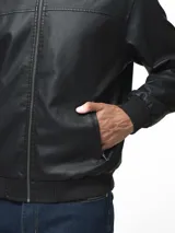 Campera tipo bomber de cuero sintético color negro, con cierre frontal completo, bolsillos laterales con cierre y puños, cuello y ruedo de tejido acanalado.