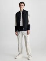 Chaleco negro acolchado con cuello alzado, cierre de cremallera, bolsillos con botón a presión y logo de Calvin Klein en el pecho.