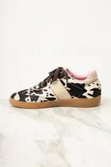 Zapatillas bajas de cuero con estampado de vaca en blanco y negro, cordones marrones y suela de goma color caramelo.
