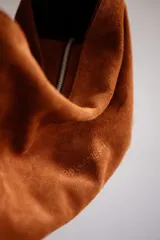 Bolso tipo hobo de gamuza color naranja quemado, con correa ancha de tela color bordó.