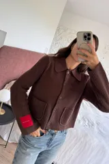 Cardigan negro de punto acanalado con cuello camisero, cierre frontal de botones y dos bolsillos delanteros. Presenta una etiqueta distintiva en la manga.