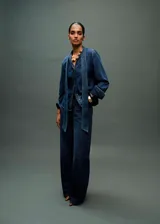 Camisa de jean con cuello camisero y lazo integrado en el frente. Presenta cierre frontal con botones, mangas largas con puños rectos y un corte recto clásico.