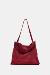 Bolso de hombro confeccionado en serraje color bordó, con diseño de tira entrelazada en la parte frontal, asa larga y cierre mediante botón imantado.