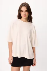 Remera de corte oversize color beige, con cuello redondo y detalle de bordado sutil en el pecho. Presenta mangas cortas con caída relajada.
