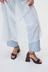 Sandalias de cuero negro con plataforma y tacón cuadrado alto. Presentan una tira delgada sobre los dedos y pulsera tobillera con hebilla dorada.