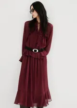 Vestido largo bordó de poliéster, de corte oversize, con escote en V y detalle de volantes en la cintura y el canesú. Cuenta con mangas largas y forro interior.