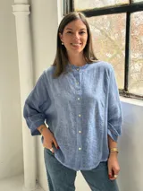 Camisa azul de lino con cuello mao, cierre frontal con botones y mangas largas abullonadas con puños elásticos.