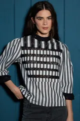 Blusa de algodón a rayas verticales en blanco y negro, con detalles de encaje negro en el pecho, cuello y puños. Presenta mangas 3/4 con terminación de encaje.