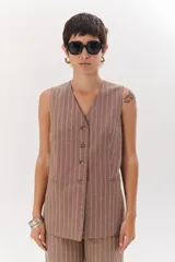 Chaleco largo color blanco con rayas verticales finas color beige, con cuello en V y cierre frontal con botones marrones. Incluye pañuelo al cuello con estampado de lunares y rayas.