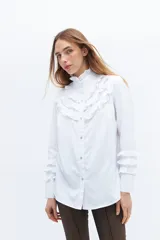 Camisa blanca de algodón con cuello alto, cierre frontal de botones y detalles de volados con broderie en el pecho y en los puños.
