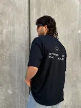Remera negra de corte oversize con estampado en la espalda que dice 'REAL ADVENTURE STORIES OF THE EAST'.