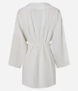 Vestido corto de playa confeccionado en voil de algodón BCI color blanco, con escote en V con lazo, cutouts laterales, mangas largas y bordados de caracoles de mar.