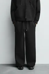 Pantalón de corte wide fit confeccionado en tejido técnico con efecto neopreno. Presenta cintura elástica ajustable con cordón, perneras anchas con costura frontal, bolsillos laterales y bolsillos traseros de plastrón.