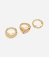 Kit de tres anillos dorados de metal reciclado, que incluye dos anillos lisos de diseño limpio y un anillo bold con piedra de cristal facetada en tono salmón.