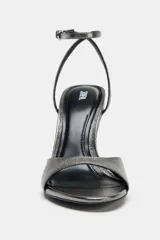 Sandalia plateada de tacón fino, con tira ancha en la parte delantera y pulsera al tobillo con cierre de hebilla metálica. Zapato con acabado en punta y efecto metalizado.