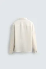 Camisa de corte regular fit confeccionada en tejido de algodón con textura de cuadrillé. Presenta cuello solapa, manga larga con puños abotonados y cierre frontal mediante botonadura.