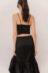 Pollera midi de tafeta color negro, con diseño asimétrico de corte mullet (más corta adelante y larga atrás), tiro alto y detalle de volado fruncido en el ruedo.