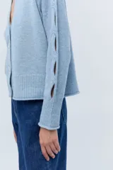 Cárdigan corto celeste de lana con lentejuelas, escote en V, cierre frontal con botones y mangas largas con aberturas.