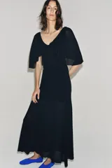 Vestido largo de punto color negro, con escote en V pronunciado tanto en el delantero como en la espalda, y mangas cortas anchas con vuelo.