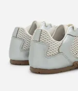 Championes de estilo urbano inspirados en botines de fútbol, confeccionados en poliuretano plateado con paneles de malla transpirable. Presentan cierre con cordones, punta redondeada y suela plana de goma en color marrón.