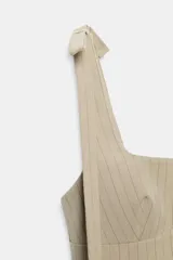 Vestido corto de punto acanalado en color beige, con escote cuadrado y tirantes con detalle de lazos. Presenta un diseño ajustado y cierre posterior con cremallera oculta.