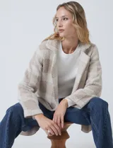 Chaqueta de tejido suave con estampado a cuadros en tonos beige y blanco, cuello con solapa y cierre de botón frontal. Incluye bolsillos delanteros.