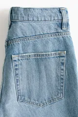 Jean tobillero de cinco bolsillos en denim de algodón rígido, con piernas de volumen curvo, tiro alto y cierre de botones.