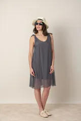 Vestido corto de seda color gris oscuro, con escote redondo y tirantes anudados en los hombros. El calce es suelto y la tela es ligeramente transparente.
