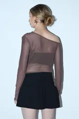 Remera de manga larga y escote asimétrico, confeccionada en tul negro transparente. Lleva un top negro opaco debajo y un cinturón de cadena plateada a la altura de la cadera.