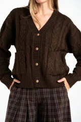 Cardigan de punto con diseño de trenzas, color marrón oscuro, con escote en V, cierre frontal de botones dorados y bolsillos delanteros.